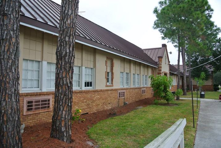 A single-story brick building with multiple windows, surrounded by trees and a well-maintained lawn.