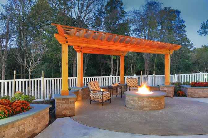 An inviting outdoor patio featuring a pergola, fire pit, and comfortable seating set against a natural backdrop during the evening.