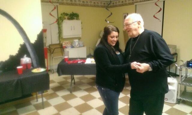 A young woman and an elderly man dancing together at an indoor gathering.