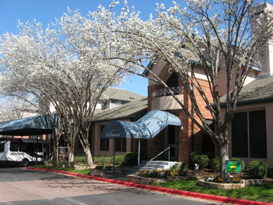 A residential building with blooming trees and a blue awning in spring.