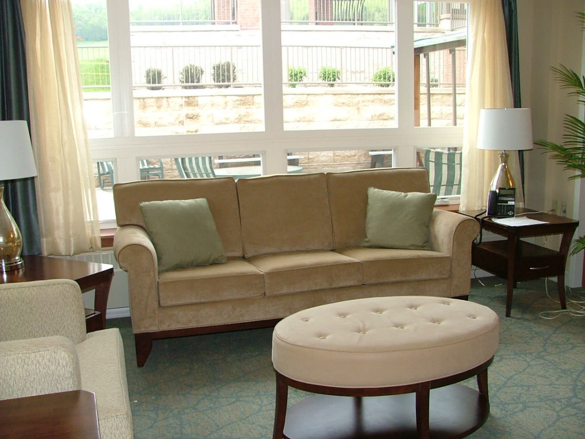 A cozy living room with a beige sofa, cushions, and an oval coffee table, bathed in natural light from large windows.