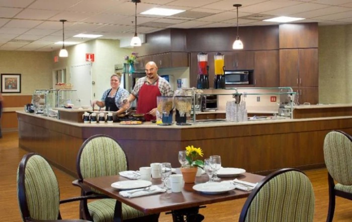 Chefs preparing food in a restaurant kitchen with neatly set tables in the foreground.