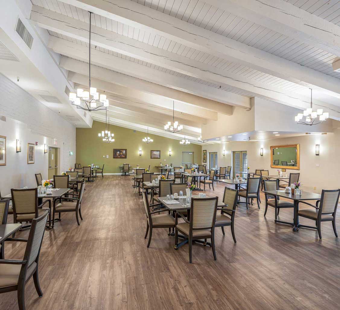 A spacious dining area with elegant chandeliers and neatly arranged tables and chairs on a wooden floor.
