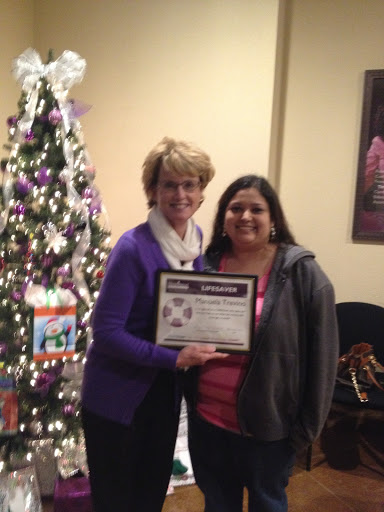 Two women proudly holding an award in front of a decorated Christmas tree.