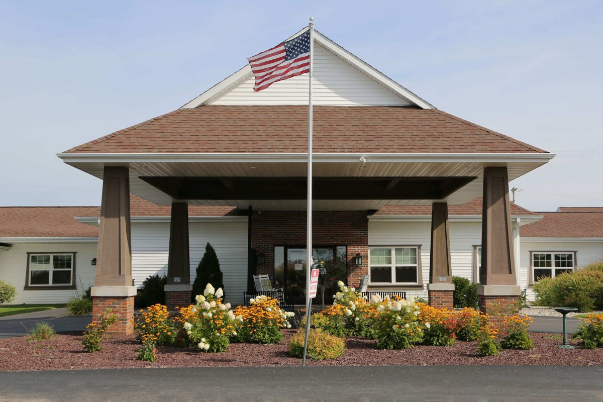 Entrance of a building with an American flag and landscaped flowers.