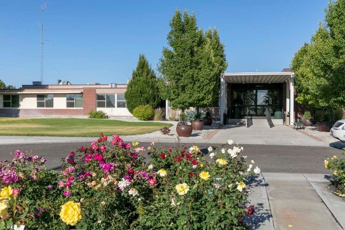 A sunny day view of a building entrance with a vibrant garden in the foreground.
