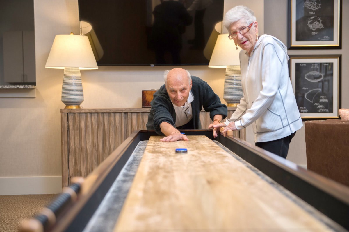 An elderly couple enjoying a game of shuffleboard indoors.