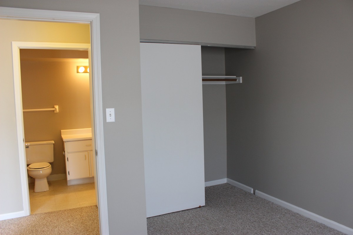 An empty room with a sliding closet door and a view into a bathroom.