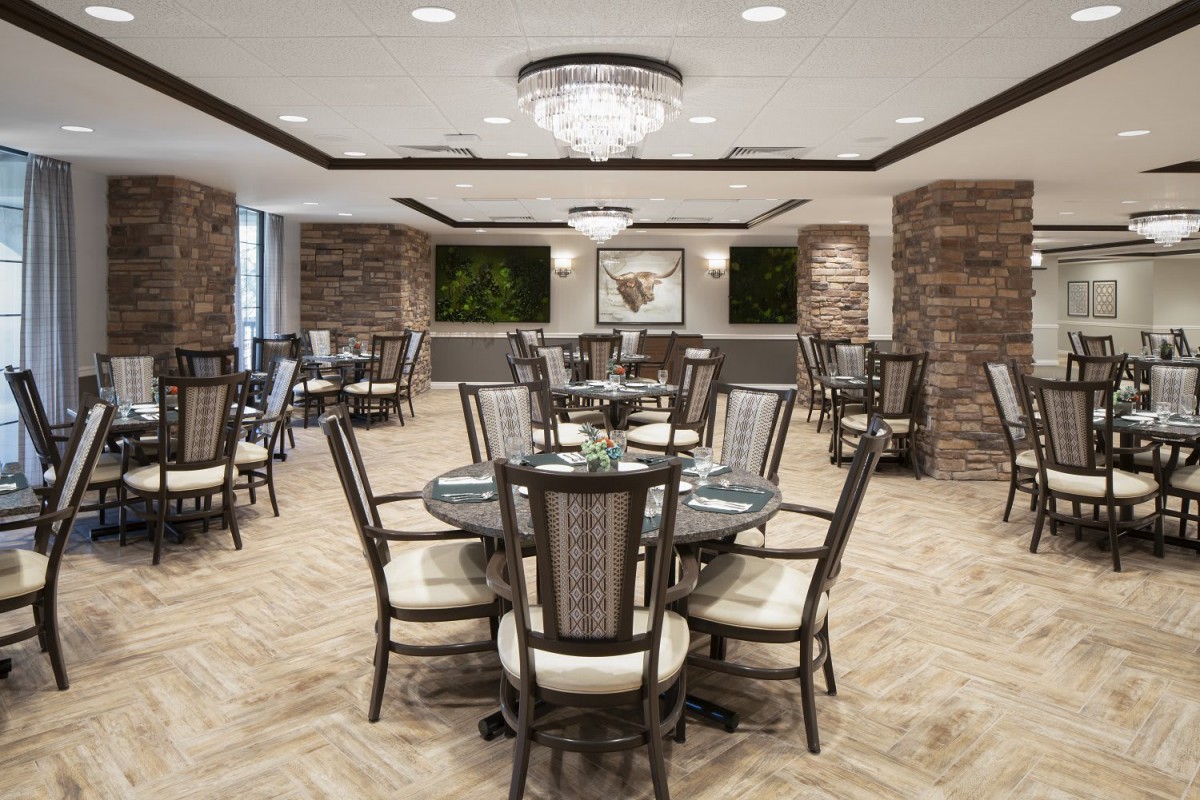An elegant dining room with modern decor, featuring multiple tables and chairs under a chandelier.