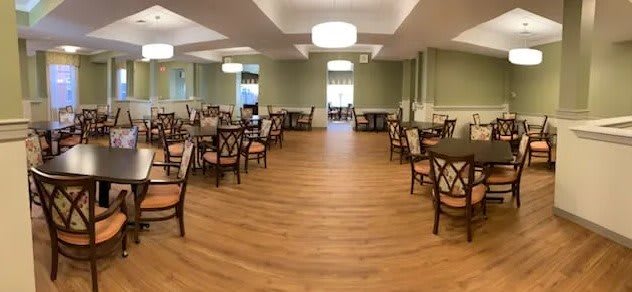 An empty dining room with arranged tables and chairs, featuring wooden flooring and elegant lighting.