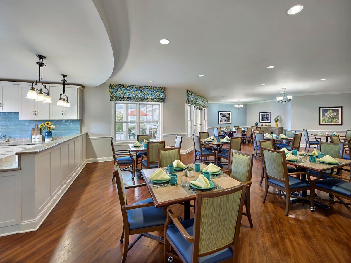 A cozy dining area with neatly arranged tables and chairs, featuring wood flooring and large windows.