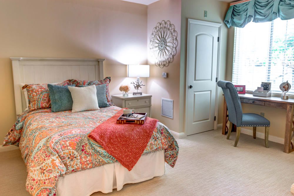 A cozy bedroom with colorful bedding, a bedside lamp, and a small desk by the window.