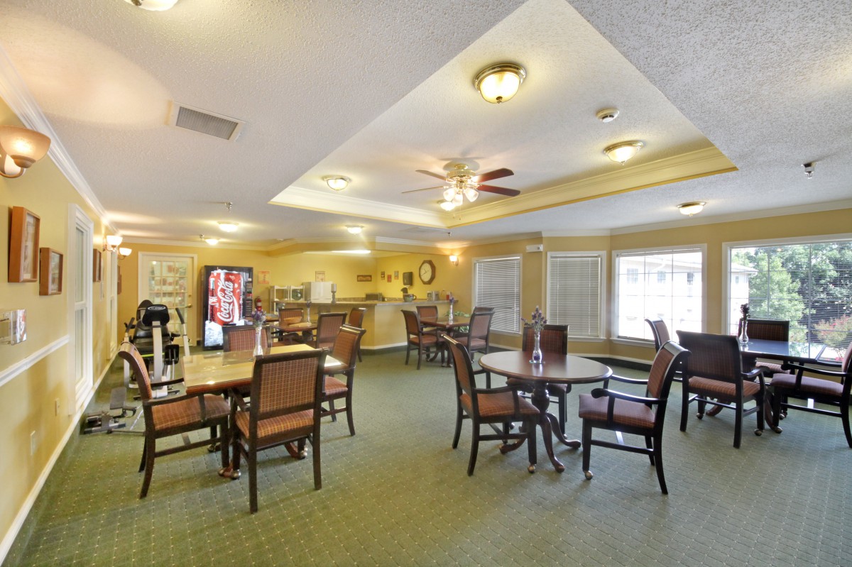 A spacious dining area with tables, chairs, and a beverage machine, complemented by warm lighting and carpeted flooring.