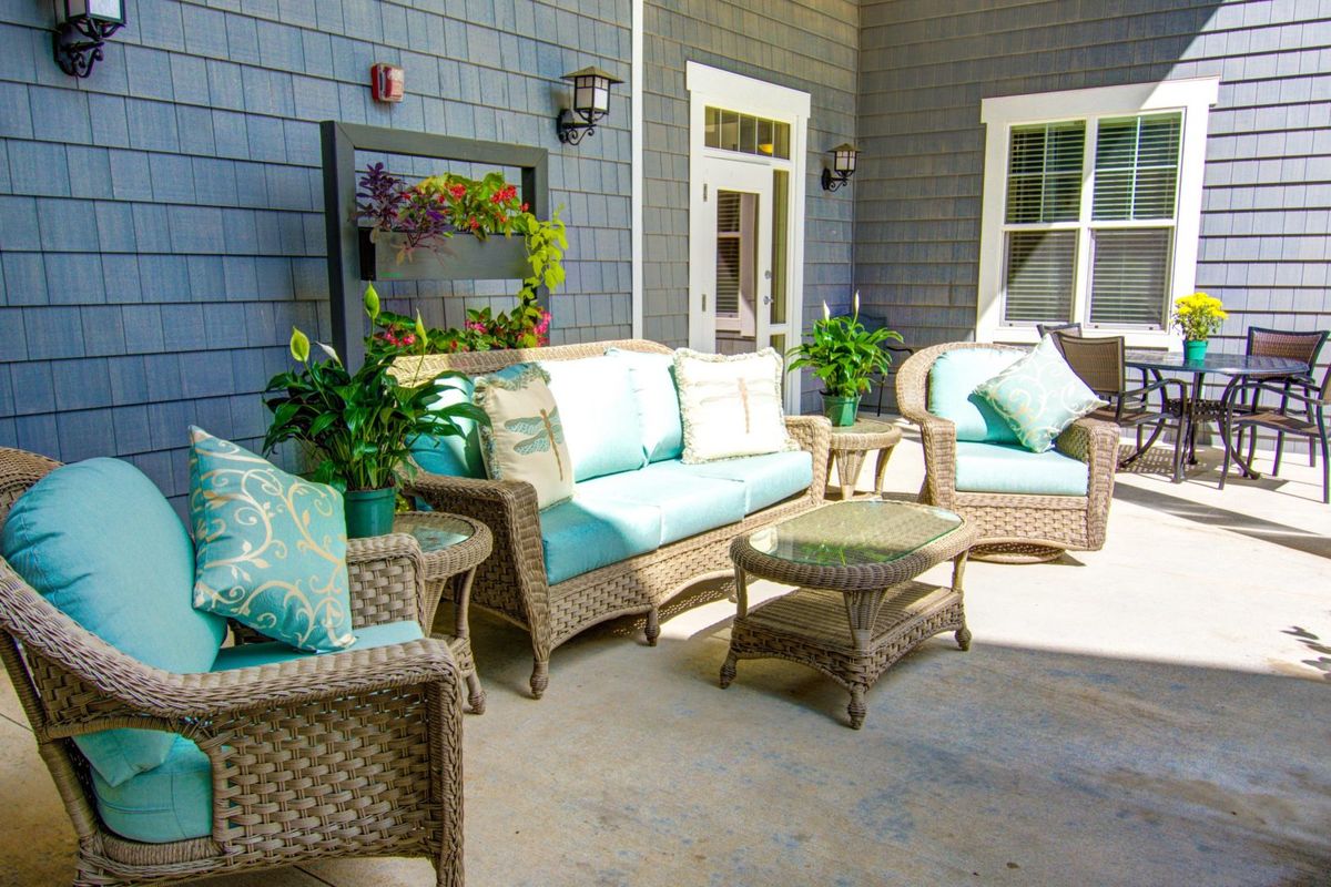 A cozy patio featuring wicker furniture with blue cushions, surrounded by potted plants.