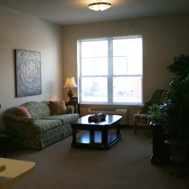 A cozy living room with a sofa, coffee table, and large window letting in natural light.