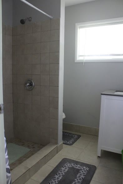 A bathroom featuring a tiled shower and a sink beneath a window.