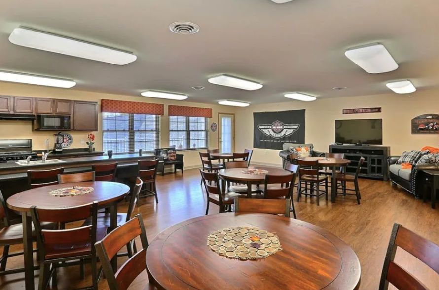 A cozy dining area with neatly arranged tables and chairs, featuring wooden flooring and ample natural light.