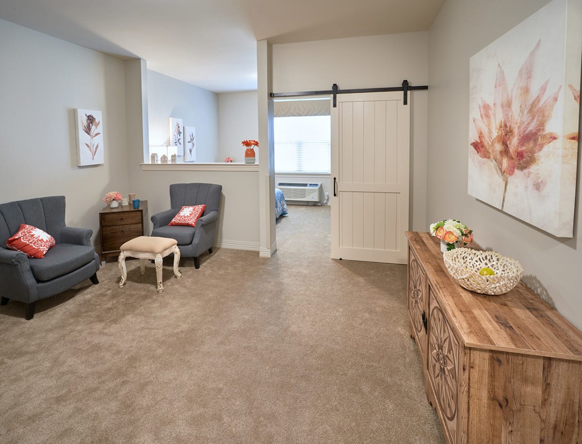 A cozy, elegantly designed living room featuring comfortable armchairs, a rustic wooden console table, and a sliding barn door leading to another space.
