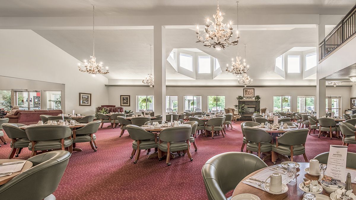 Spacious dining room with elegant chandeliers and large windows, featuring round tables and comfortable chairs.