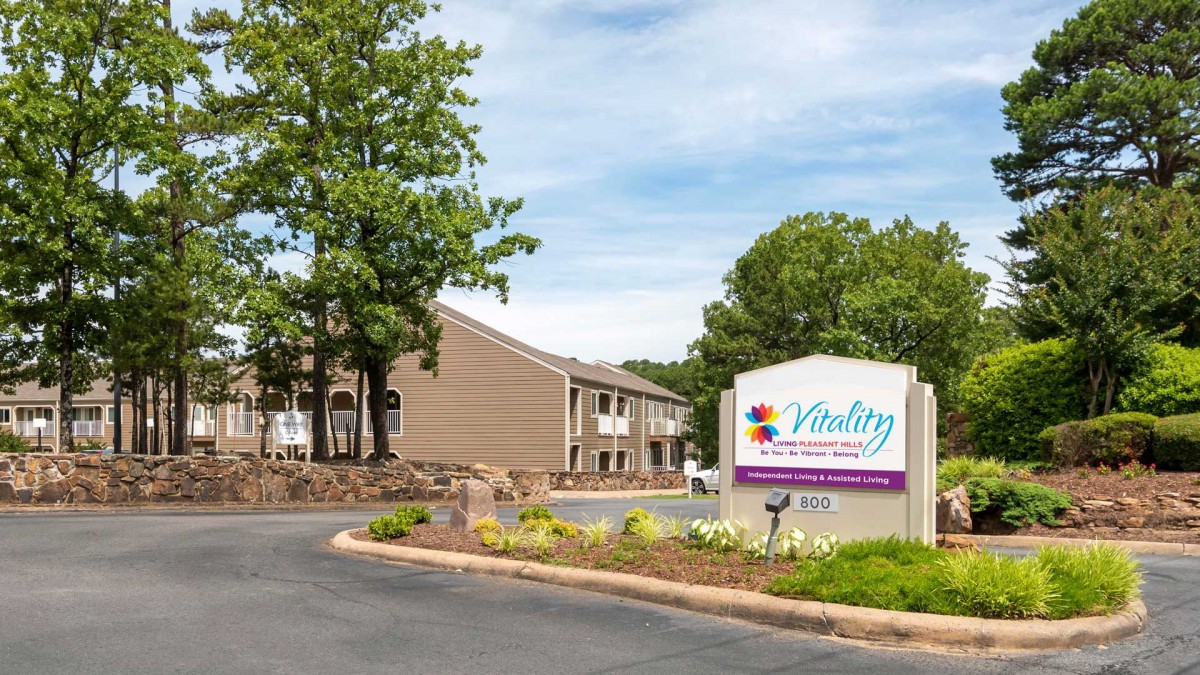 Exterior view of a building with a welcome sign and landscaped driveway.