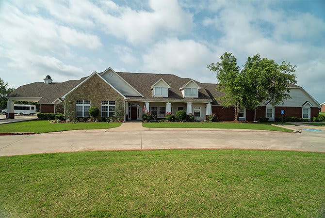A large suburban house with a well-maintained lawn and driveway under a cloudy sky.