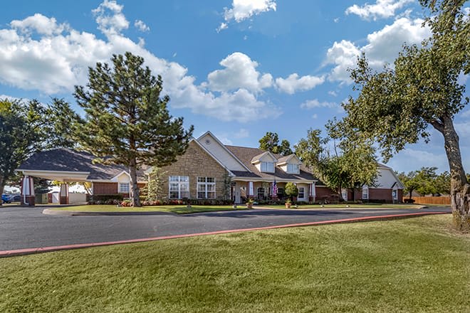 A suburban house surrounded by trees and a well-maintained lawn under a partly cloudy sky.