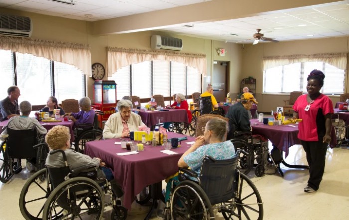 Seniors in wheelchairs gather in a nursing home's dining room for a meal and social interaction.