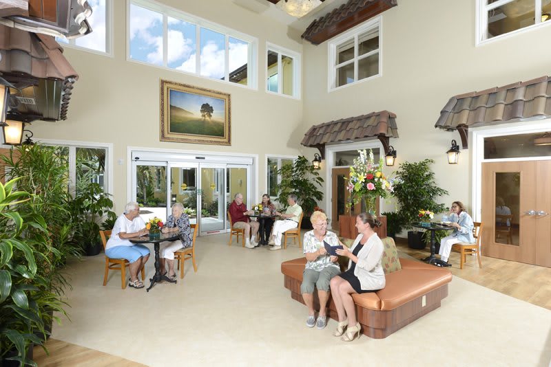 A spacious lobby with people engaging in conversations, surrounded by furniture and greenery.