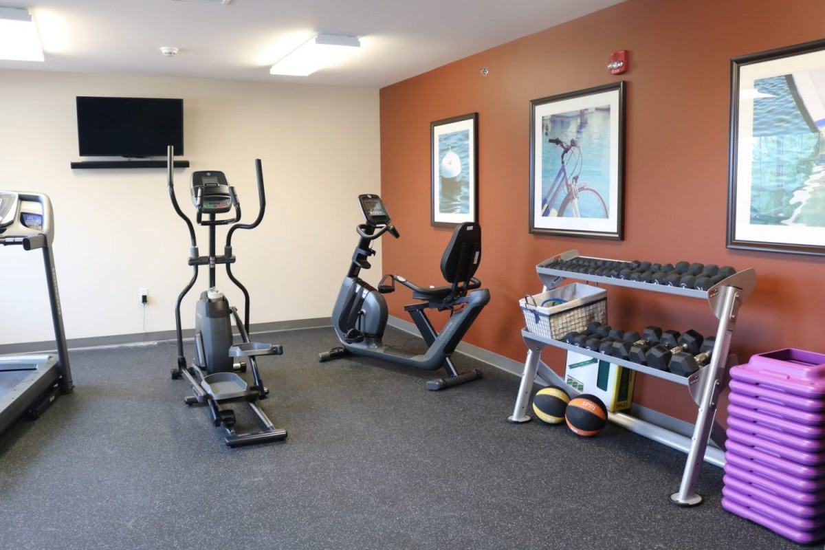 A small gym with essential fitness equipment including an exercise bike, elliptical machine, and a rack of dumbbells.