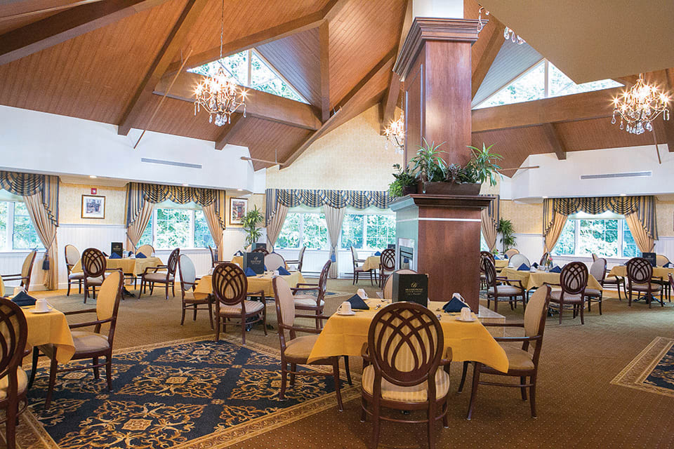 An elegant restaurant interior with wooden ceilings, chandeliers, and well-arranged dining tables.