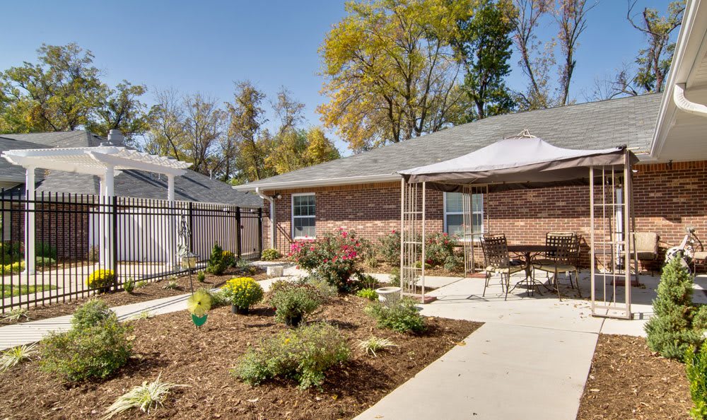 A well-maintained backyard featuring a garden with various plants, a paved path, and outdoor seating under a canopy on a sunny day.