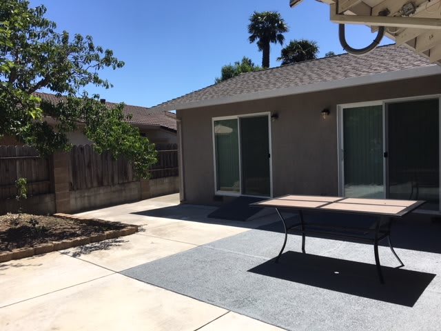 A sunny backyard patio with outdoor furniture and sliding glass doors.