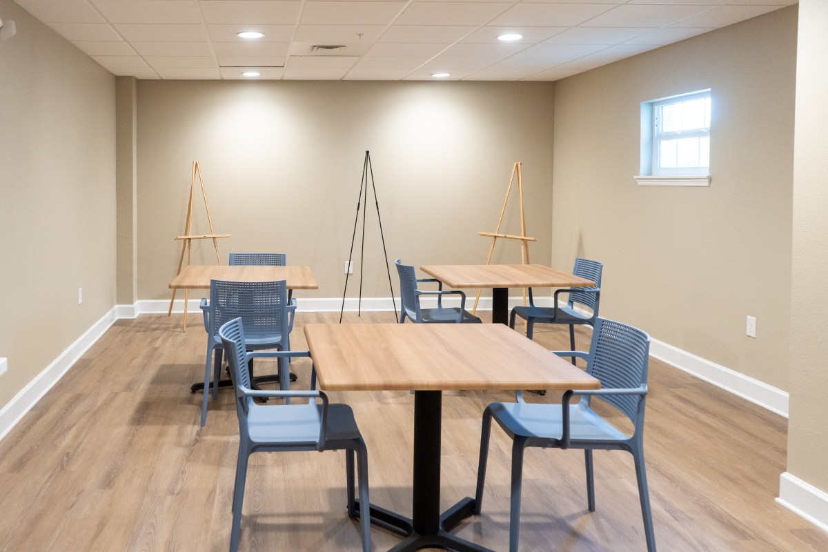 An art studio with tables, chairs, and easels arranged on a wooden floor.