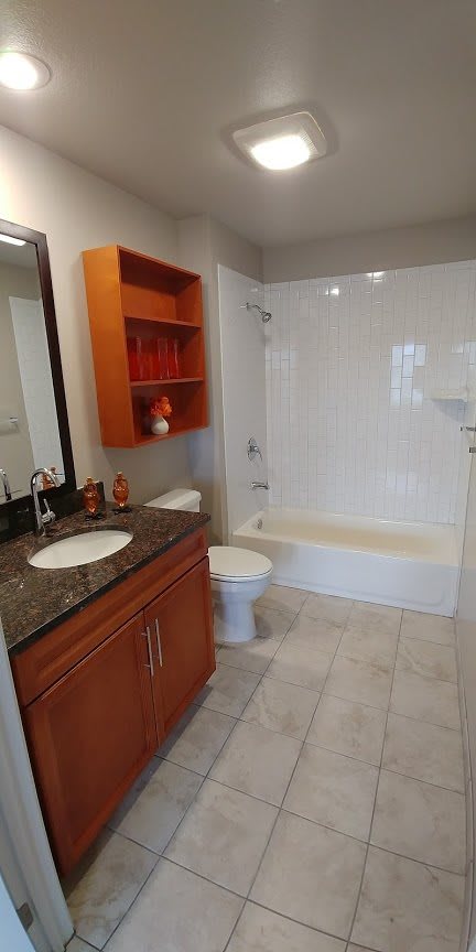A modern bathroom with a granite countertop, wooden cabinets, and a clean white bathtub.