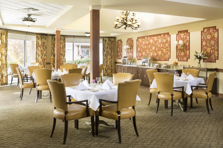 An elegant dining room with neatly arranged tables and chairs, adorned with white tablecloths and decorative lighting.