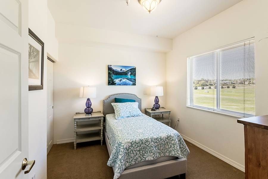 A cozy bedroom with a single bed, flanked by nightstands and lamps, featuring a window and wall art.