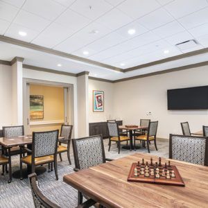 A well-lit game room featuring a chess board, multiple tables and chairs, a television, and artwork on the walls.