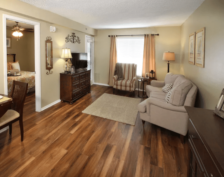 A cozy living room with wood flooring, featuring a comfortable sofa, chair, and a TV setup.