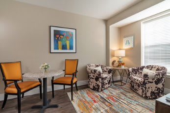 A cozy living room with colorful chairs, a patterned rug, and artwork on the wall.