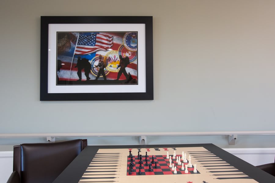 A framed painting featuring various flags hangs above a chessboard setup in a room.