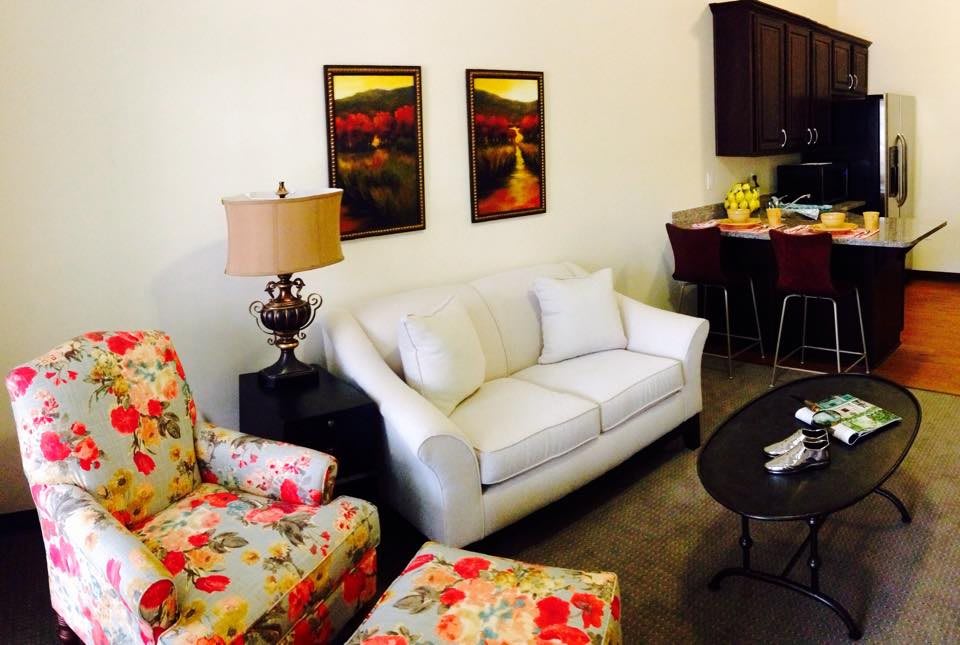 A cozy living room with a white sofa, floral armchairs, and a dining area in the background.