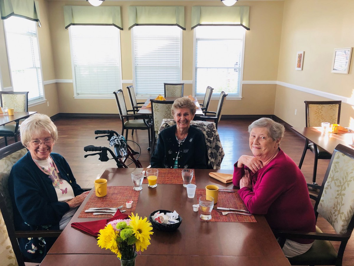 Three seniors sitting around a table in a dining room.