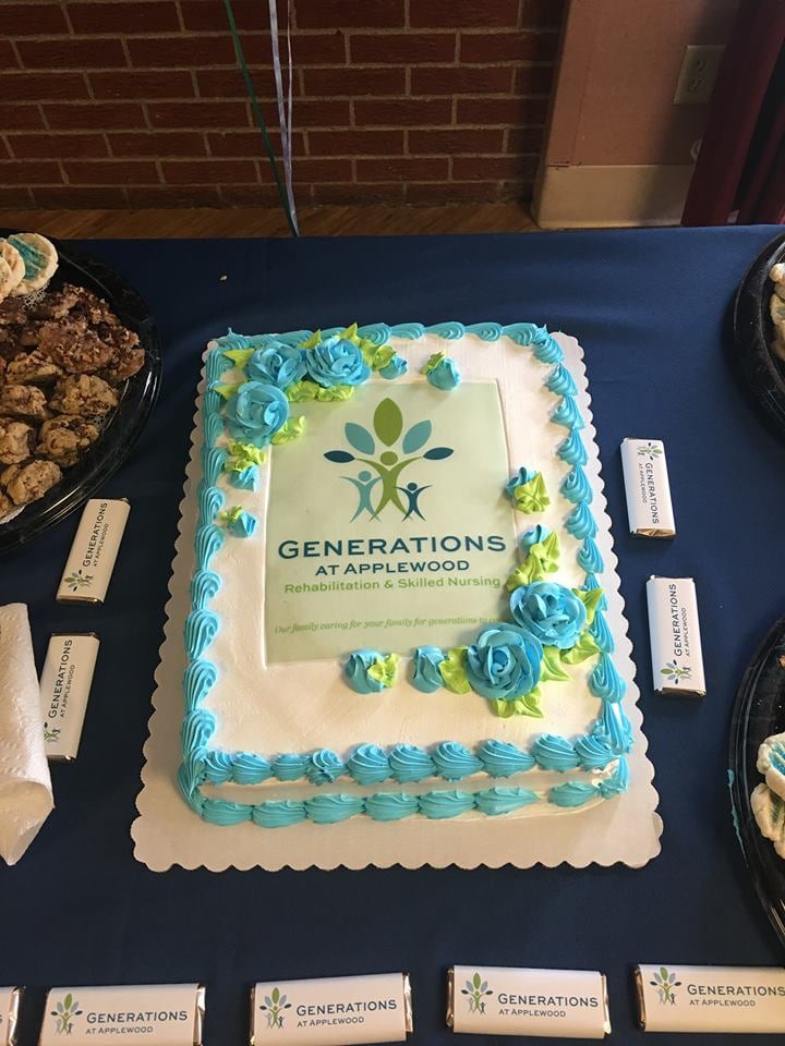 A decorated cake featuring the Generations logo, surrounded by cookies at an event.