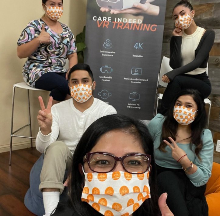 A group of people wearing masks pose together indoors with peace signs.