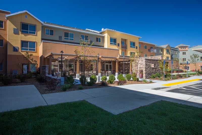 A modern residential apartment complex with well-maintained landscaping and outdoor pathways under a clear blue sky.