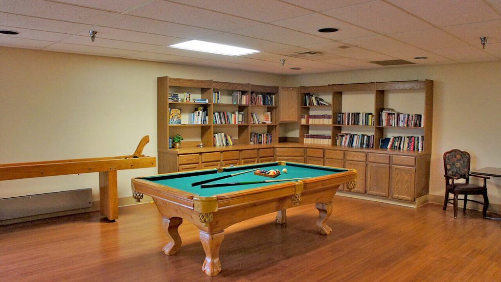 A recreation room featuring a billiard table and bookshelves filled with books.