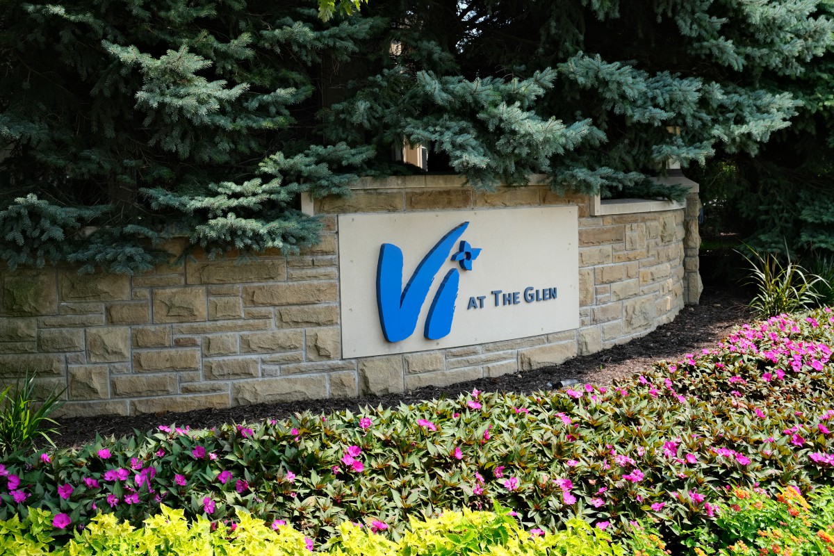 A stone sign surrounded by vibrant flowers and greenery at a building entrance.