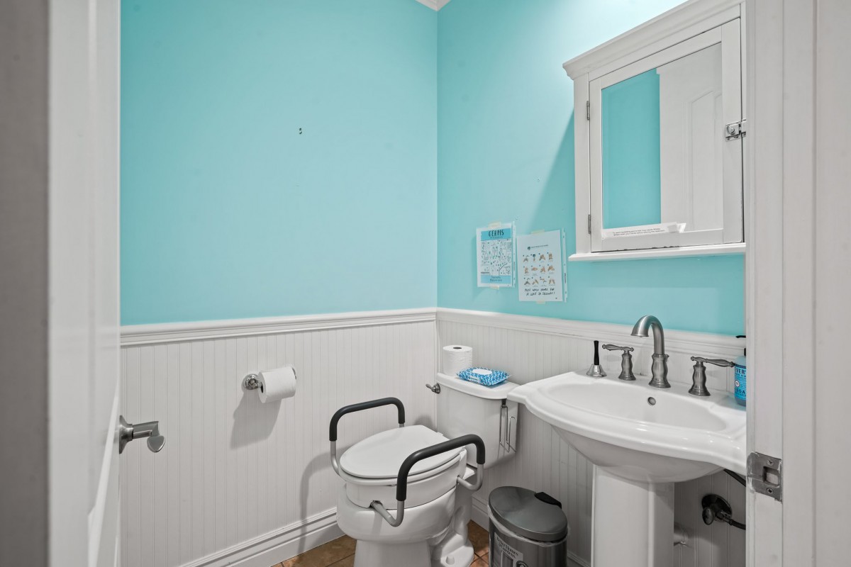 An accessible bathroom with turquoise walls, featuring a sink, toilet with handrails, and a wall-mounted mirror.