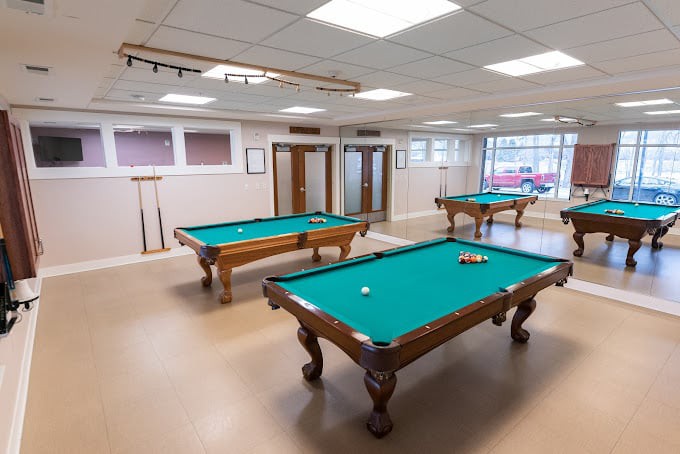 A billiard room with multiple pool tables and bright lighting.