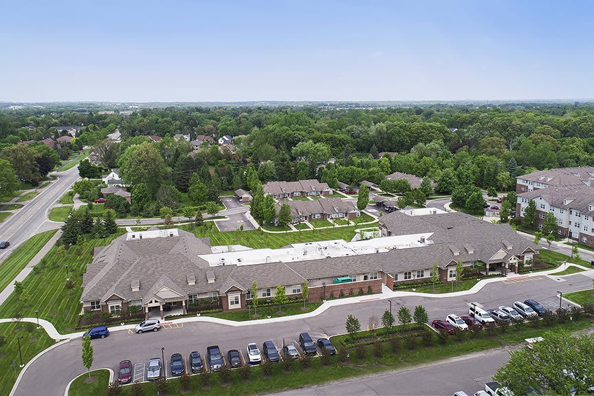 An aerial view of a suburban complex with buildings surrounded by greenery and a parking lot.